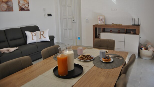 A modern living room with a sofa, dining table, and a kitchen area in the background.