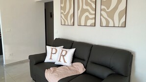 A modern living room with a dark grey sofa, two white pillows with 'PR' on them, and a beige throw blanket. Three abstract wall art pieces are hung above the sofa.
