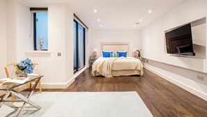 A modern bedroom with a large bed, a TV mounted on the wall, and a dining area with a table and chairs. - The Primrose Hill Elegant House (Greater London)