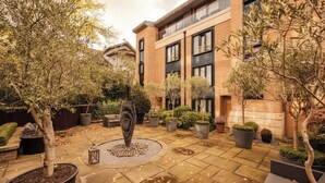 A courtyard with potted plants, a central decorative feature, and a building with large windows and a brick facade. - The Primrose Hill Elegant House (Greater London)