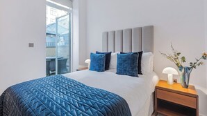 A bedroom with a large bed, a grey headboard, and a window overlooking a building.