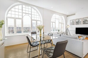 A modern living room with a glass dining table, grey sofa, and a flat-screen TV. - By Oxford Circus in Great Style (Greater London)