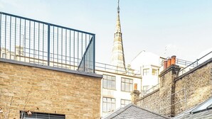 A courtyard with a brick building, a small garden, and a view of a tower.