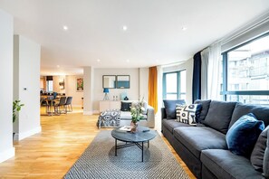 A modern living room with a grey sofa, a coffee table, and a dining area in the background. - Super Spacious Two Bedroom By London Bridge (Greater London)