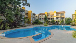 A swimming pool surrounded by a landscaped area with a multi-story building in the background. - REEMZ BEACH HEAVEN HOTEL (Anjuna)