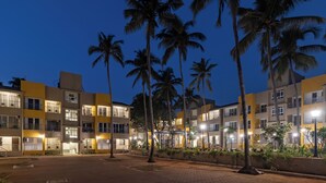 A multi-story hotel with balconies, a paved courtyard, and palm trees. - REEMZ BEACH HEAVEN HOTEL (Anjuna)