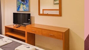 A hotel room with a bed, a wooden desk with a television, and artwork on the wall. - REEMZ BEACH HEAVEN HOTEL (Anjuna)