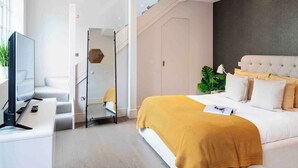 Ein modernes Schlafzimmer mit einem großen Bett, einem Schreibtisch und einem Fernseher. Eine Treppe führt zu einer oberen Ebene.
