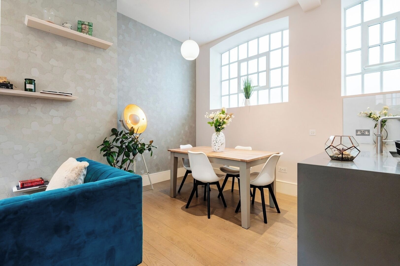 Ein modernes Wohnzimmer mit einem blauen Sofa, einem Esstisch mit Stühlen, einer Pendelleuchte und einem großen Fenster.