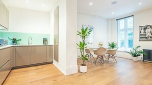 Una cocina moderna con un lavamanos, encimera y armarios. Hay una zona de comedor con mesa y sillas, y un ventanal que proporciona luz natural.