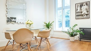 Un área de comedor moderna con una mesa de vidrio y sillas de madera, un espejo decorativo y un ventanal con vistas.