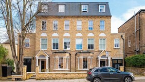 A two-story brick building with a car parked in front. - All in One Gardened Flat (Greater London)