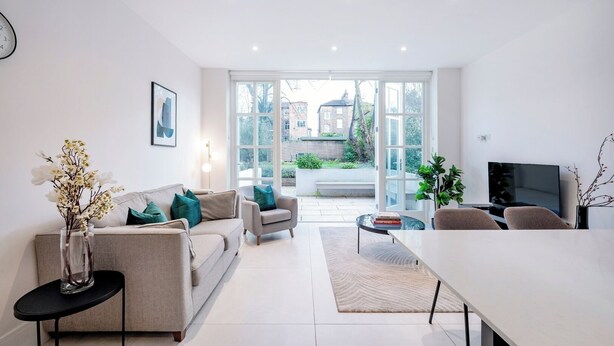 A modern living room with a sofa, armchairs, a coffee table, and a TV. - All in One Gardened Flat (Greater London)