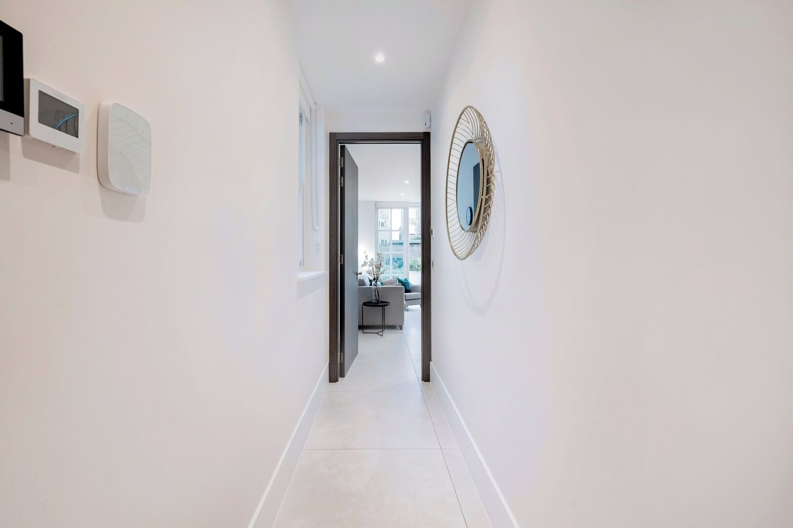 Un couloir moderne aux murs blancs, agrémenté d’un grand miroir et d’une porte donnant sur un espace de vie.