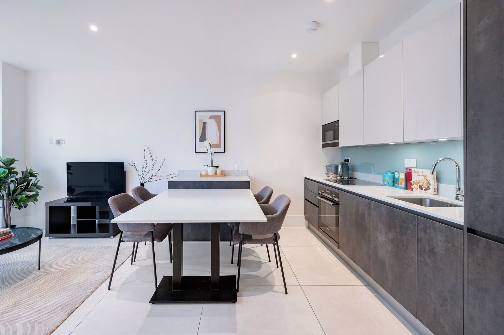 A modern kitchen with a dining area, featuring a large table, chairs, and a TV.