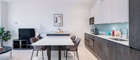 A modern kitchen with a dining area, featuring a large table, chairs, and a TV.