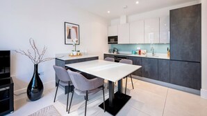 A modern kitchen with white cabinets, a black countertop, and a dining area with a white table and grey chairs. - All in One Gardened Flat (Greater London)