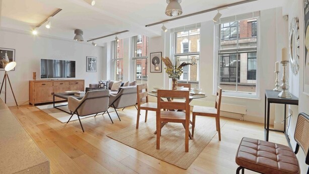 A spacious living room with a large TV, wooden furniture, and large windows offering views of the city.