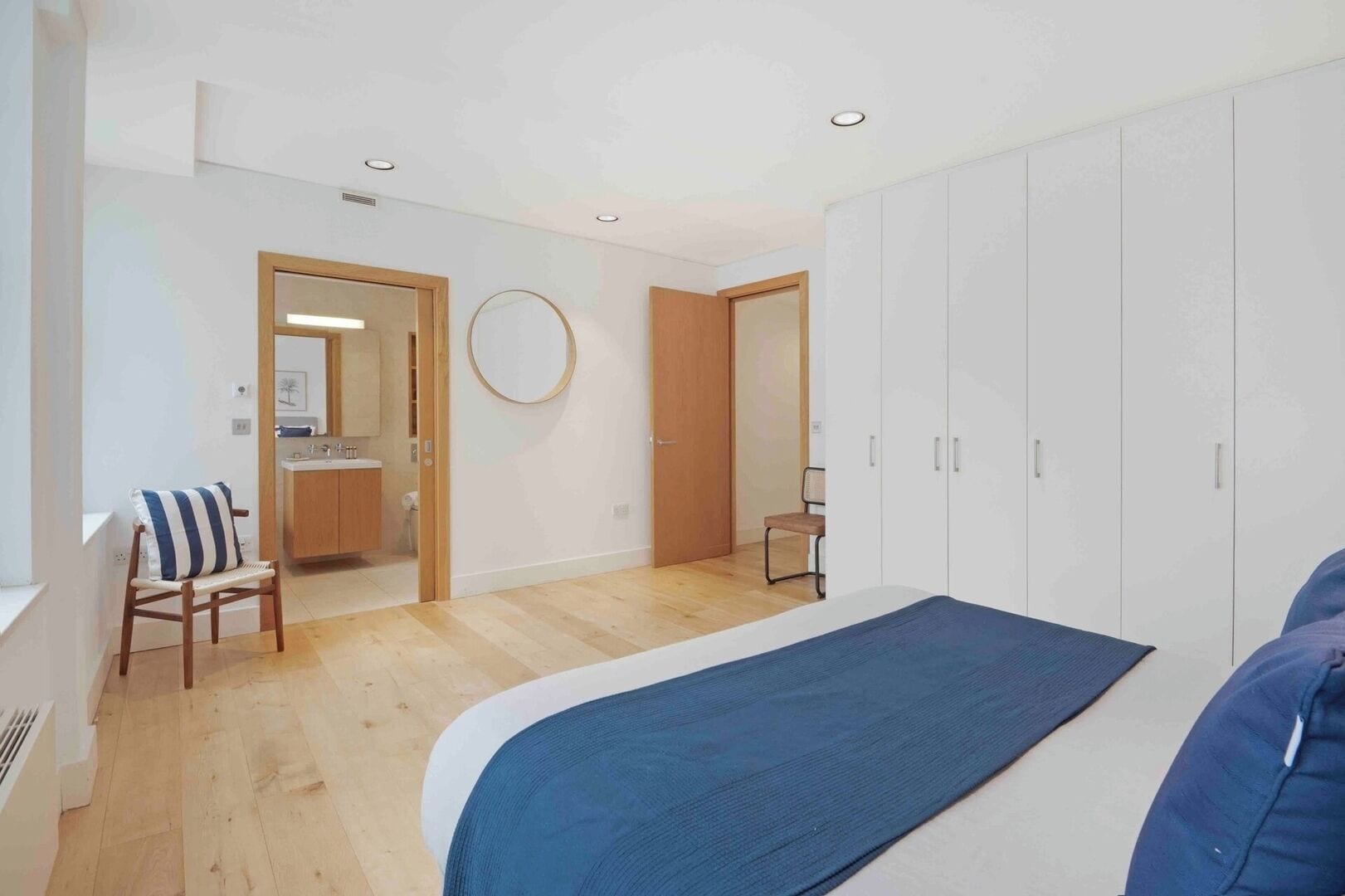 A bedroom with a bed, a chair, a wardrobe, and a bathroom visible through an open door.