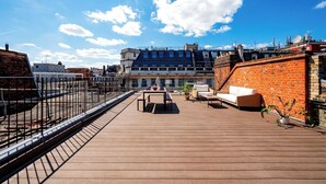 A rooftop terrace with a wooden deck, outdoor furniture, and a brick wall. - Soak in the Spalike Marble Bath at Plush Penthouse (Greater London)