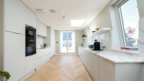 A modern kitchen with white cabinets, a black oven, and a window with books on the windowsill. - Soak in the Spalike Marble Bath at Plush Penthouse (Greater London)