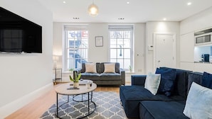 Un salon moderne avec un canapé bleu foncé, une table basse ronde et un téléviseur fixé au mur.
