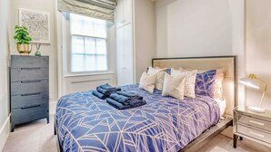 A bedroom with a bed, a dresser, a window with a view, and a bedside lamp. - The Cosy Compact flat in Mayfair (Greater London)