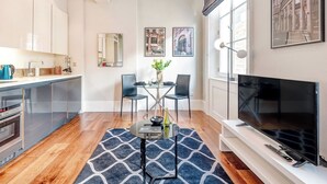 A modern kitchen with a dining area, a TV, and artwork on the walls. - The Cosy Compact flat in Mayfair (Greater London)