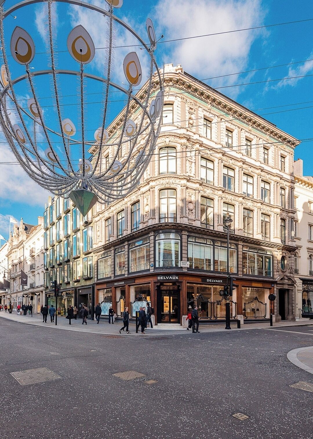 A historic building with multiple Delvaux store fronts, large windows, and a distinctive metal sculpture in the foreground.