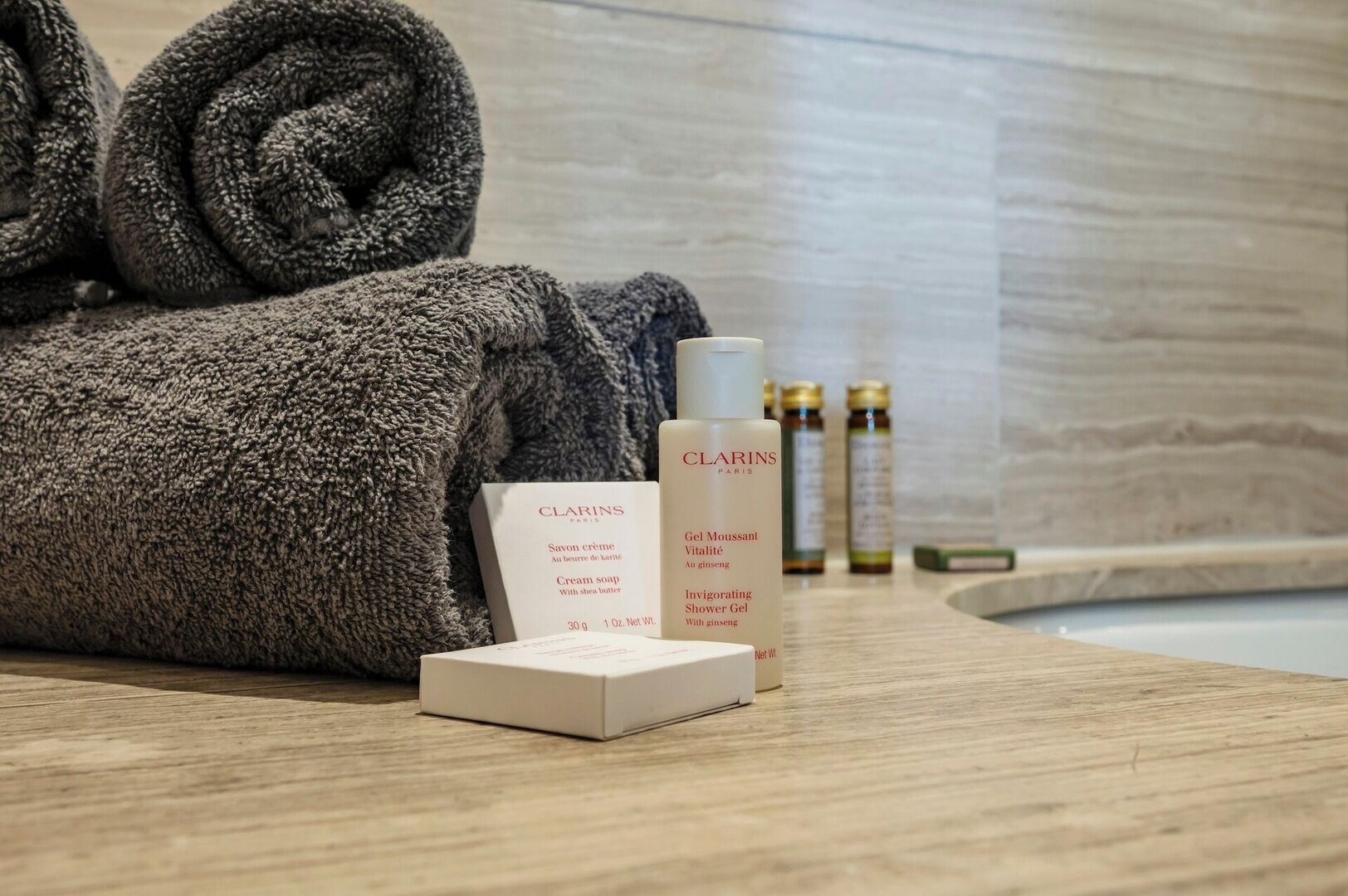 Een netjes opgevouwen handdoek, een doosje Clarins Paris crèmesoap en een fles Clarins douchegel op een houten oppervlak.