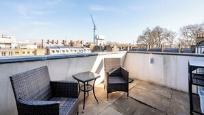 A rooftop terrace with wicker furniture, a clear view of the cityscape, and a construction crane in the distance. - Best Penthouse in Bloomsbury (Greater London)