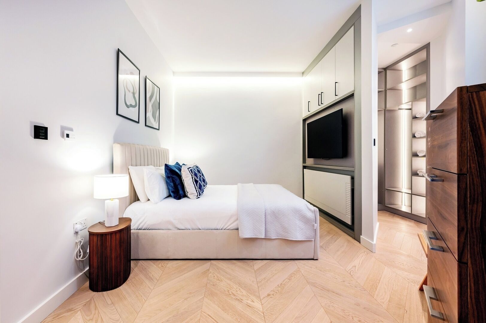 Une chambre d’hôtel moderne équipée d’un lit, d’une lampe de chevet, d’œuvres d’art, d’un téléviseur et d’un dressing.