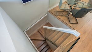 A modern staircase with wooden steps and glass railings, leading to a dining area with a glass table and chairs. - The Two Connected Penthouses (Greater London)