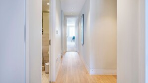 A hallway with wooden flooring, white walls, and a staircase to the left. - The Two Connected Penthouses (Greater London)