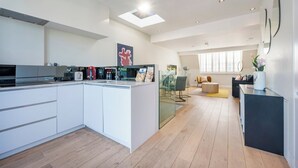A modern kitchen with a central island, a dining area with a round table, and a living space with a sofa and a coffee table. - The Two Connected Penthouses (Greater London)