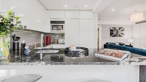 A modern kitchen with white cabinets, a black marble countertop, and a dining area with a blue sofa.