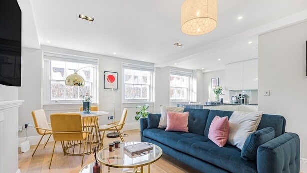 A modern living room with a blue sofa, a glass coffee table, and a dining area with yellow chairs.