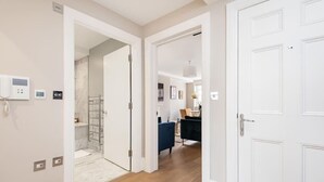 A hallway with a shower, a blue chair, and a white door.