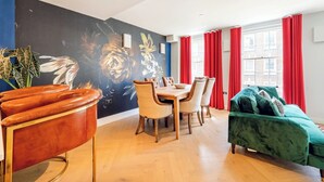 A modern living room with a dining area, featuring a large floral mural, red curtains, and a green sofa. - A Slick House Trendy Spitafields (Greater London)