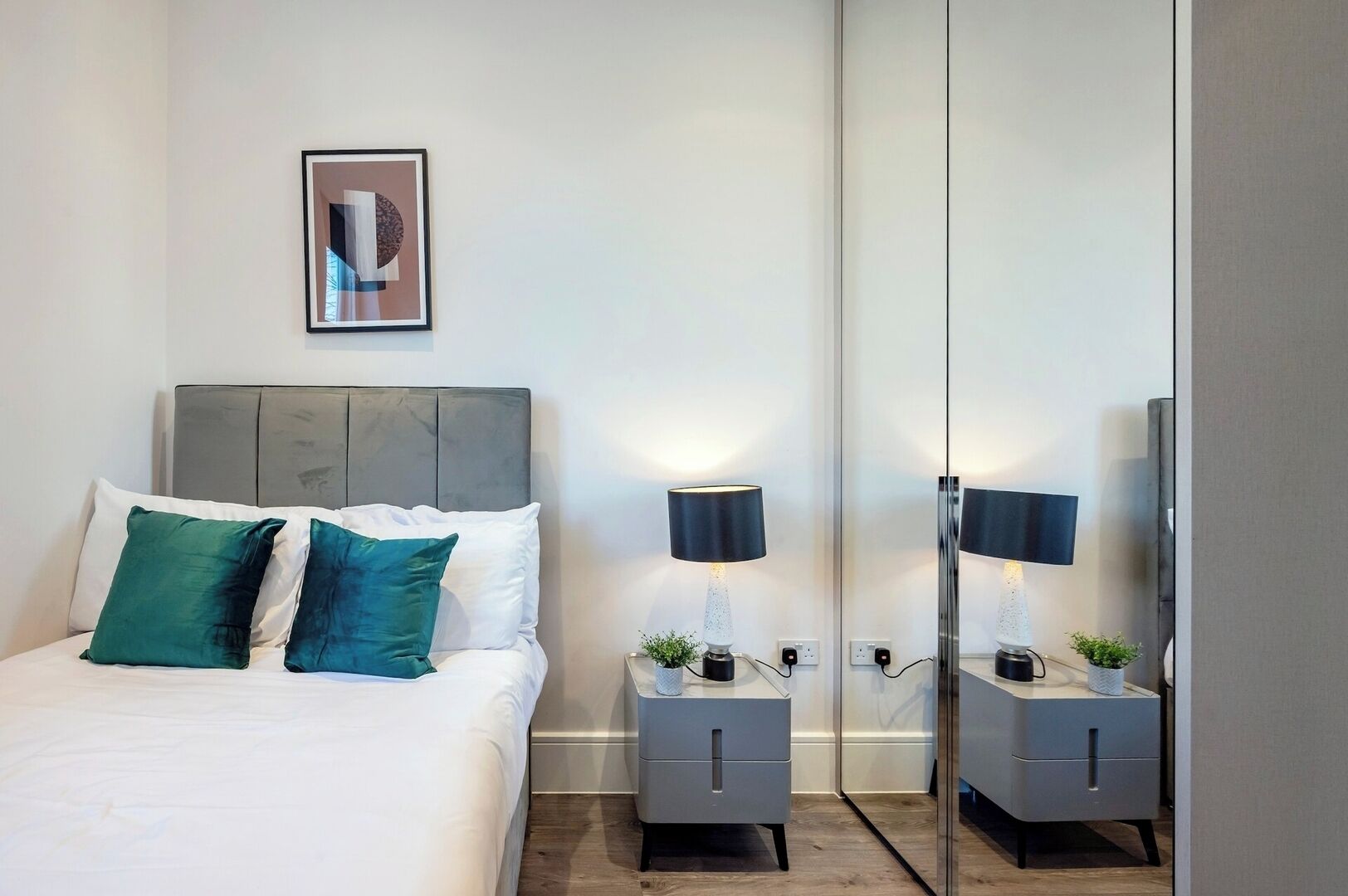 A modern hotel room with a bed, two nightstands, a lamp, and a mirror.