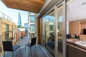Ein Balkon mit zwei Stühlen, Holzboden und Blick auf eine Stadtansicht, darunter ein hohes Gebäude.
