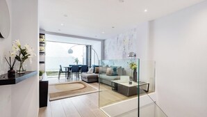 A modern living room with a glass partition, a sofa, a coffee table, and a dining area with chairs and a table.