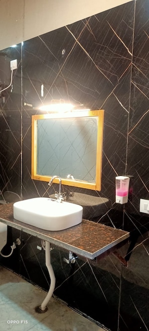 A bathroom with a white sink, a mirror with a wooden frame, and a soap dispenser.