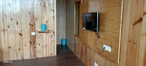 A wooden interior with a television mounted on the wall, a blue bucket on the floor, and a shelf with a blue object.