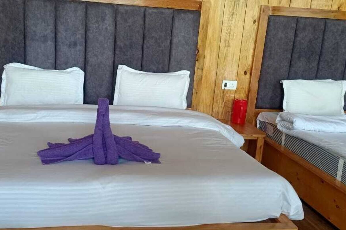 A hotel room with a large bed, two smaller beds, wooden walls, and a grey headboard.