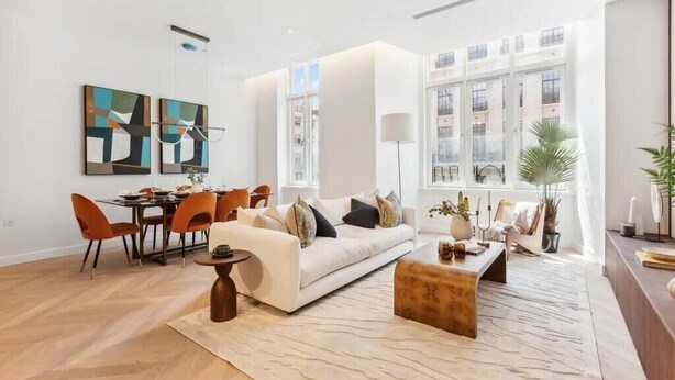 Ein modernes Wohnzimmer mit Sofa, Couchtisch und Essbereich. An den Wänden hängen zwei Gemälde, eine Stehlampe und ein großes Fenster.