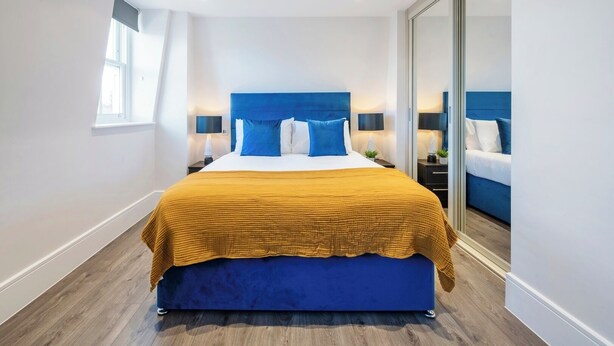 Une chambre moderne avec un grand lit, une tête de lit bleue et une porte-fenêtre coulissante donnant sur un balcon.