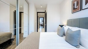 Ein modernes Schlafzimmer mit einem großen Bett, einer Glastür zu einem Flur und Blick in einen Essbereich.