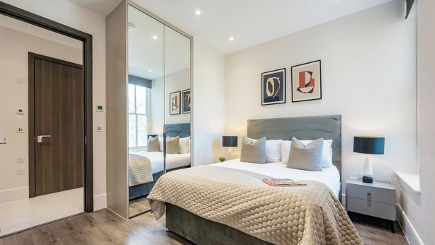 Ein modernes Schlafzimmer mit einem großen Bett, Nachttischen, einem Spiegel und Bildern an der Wand.
