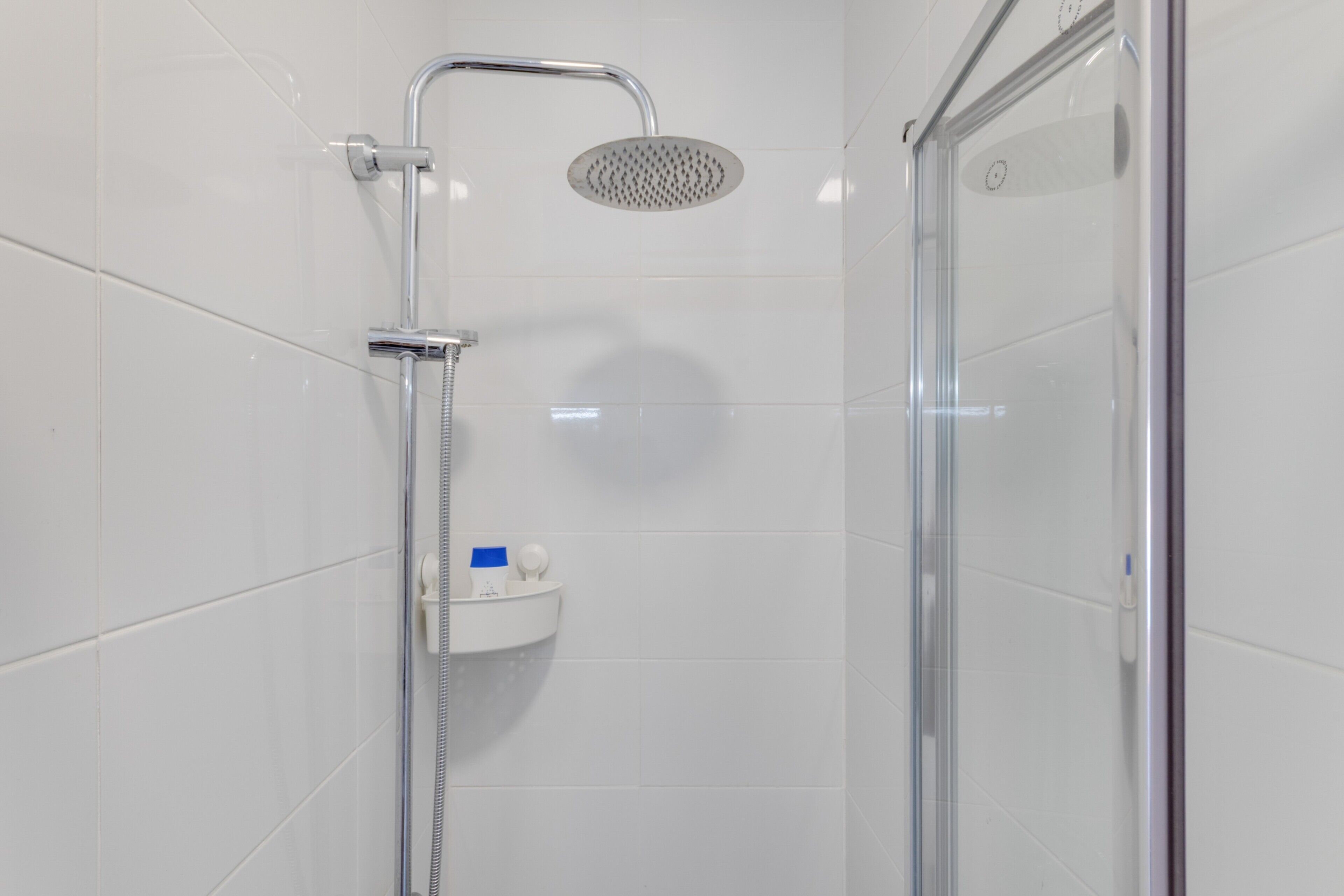 A modern shower enclosure with a handheld showerhead, a glass door, and a small shelf with toiletries.